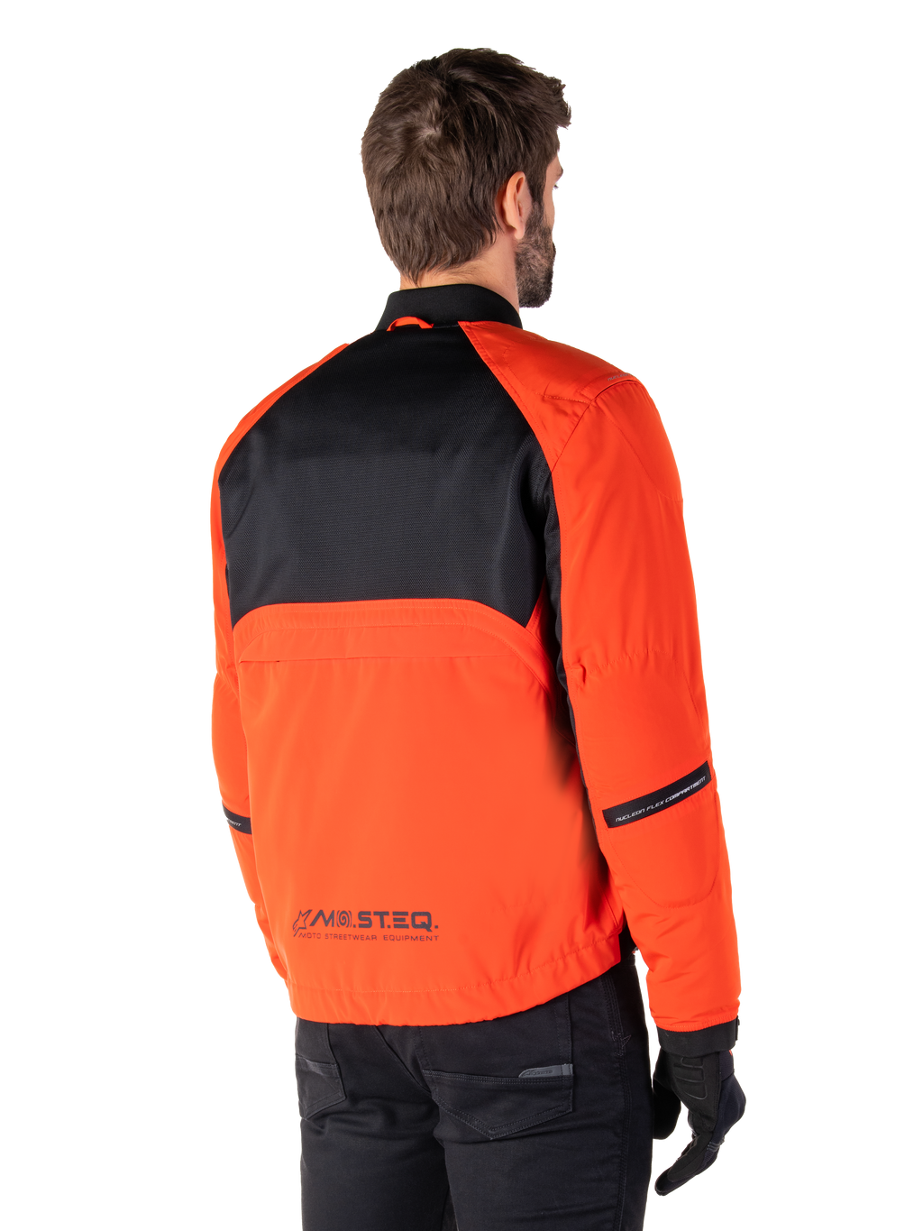 Vista posteriore di un pilota che indossa il Parka Alpinestars Mootant Waterproof in Spicy Orange e nero, caratterizzato da un pannello posteriore superiore in mesh nero e marchio riflettente MO.ST.EQ., giacca da moto moderna in stile utilitario.