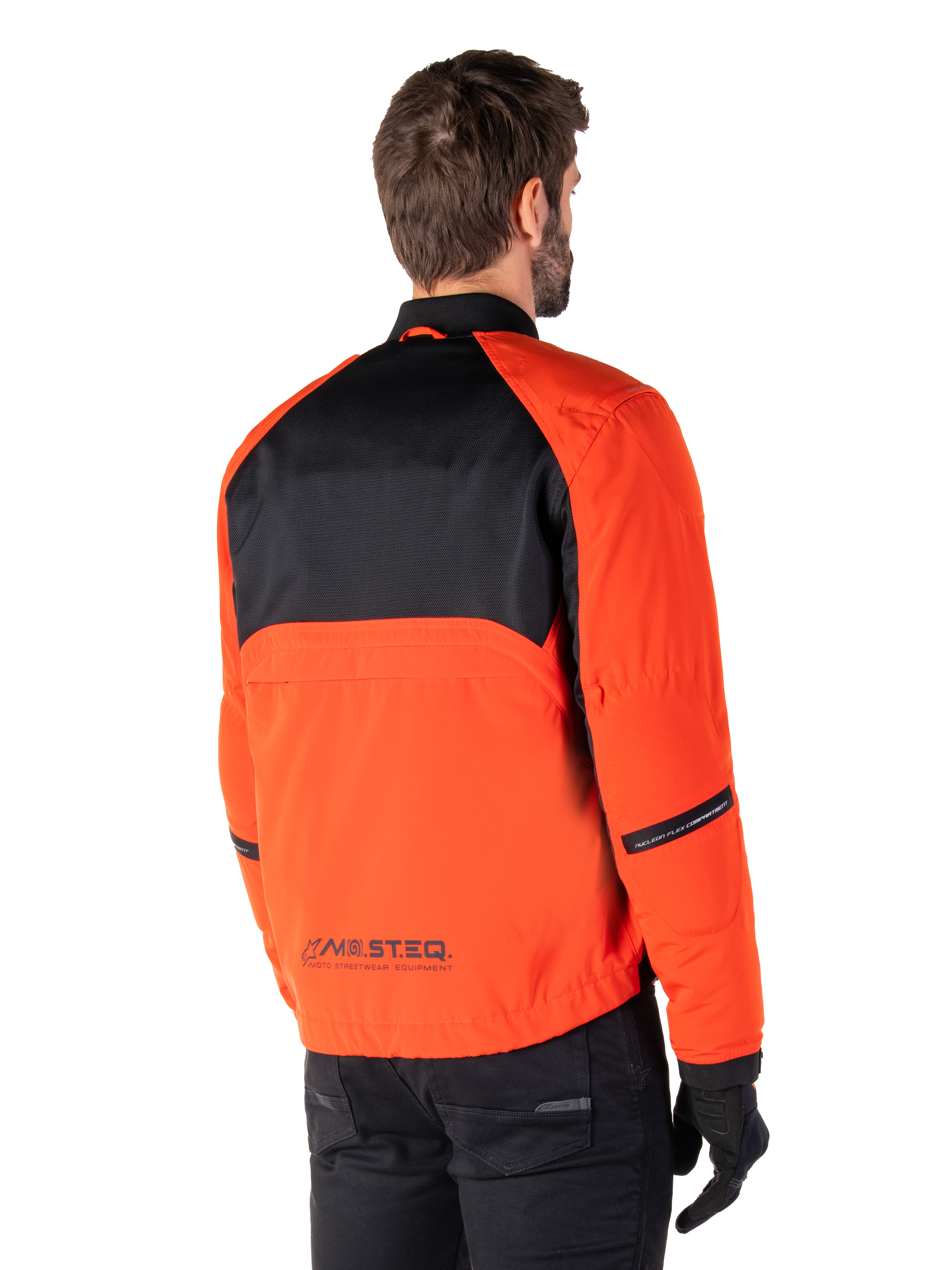 Vista posteriore di un pilota che indossa il Parka Alpinestars Mootant Waterproof in Spicy Orange e nero, caratterizzato da un pannello posteriore superiore in mesh nero e marchio riflettente MO.ST.EQ., giacca da moto moderna in stile utilitario.