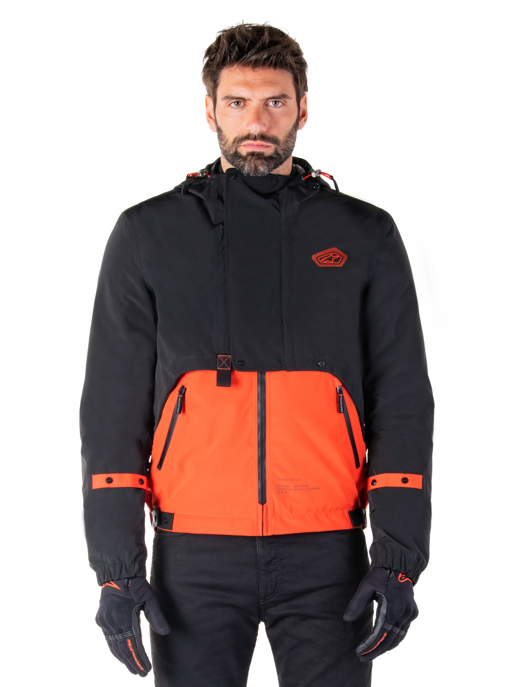 Alpinestars Mootant Waterproof Parka, giacca da moto modulare in Spicy Orange e nero, indossata da un modello con guanti coordinati, design con cappuccio e pannelli bicolore, cerniera frontale e polsini regolabili, abbigliamento tecnico urbano contemporaneo