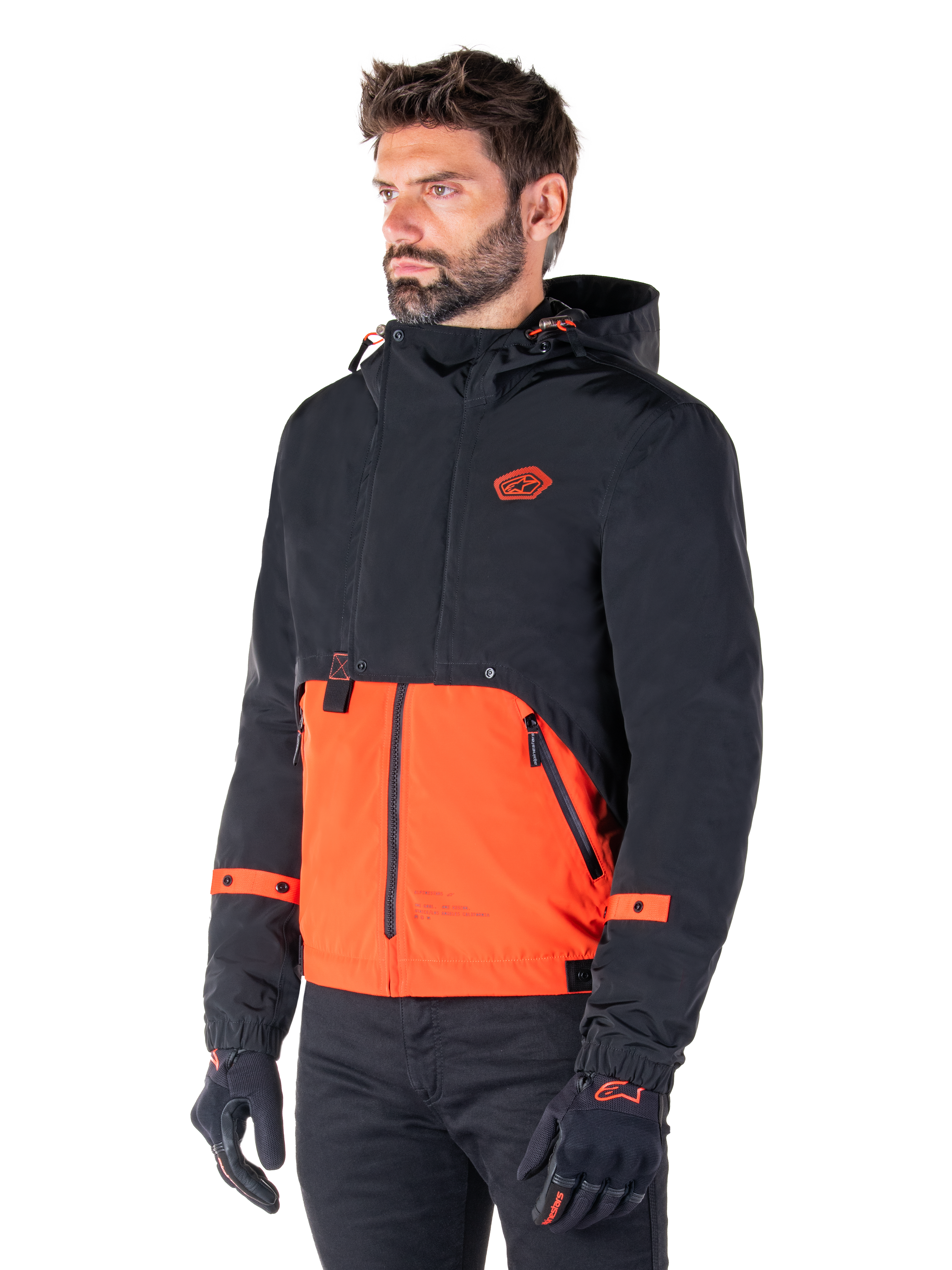 Uomo che indossa il parka impermeabile Alpinestars Mootant in Spicy Orange e nero, una giacca da moto modulare con strato superiore nero con cappuccio e sezione inferiore arancione brillante, abbinata a guanti da guida e pantaloni neri.