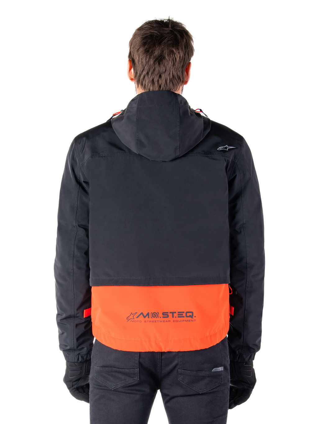 Alpinestars Mootant Waterproof Parka in Spicy Orange e nero, vista posteriore che mostra la parte superiore nera con cappuccio e il pannello inferiore arancione con il marchio MO.ST.EQ., streetwear funzionale da moto