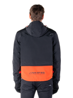 Alpinestars Mootant Waterproof Parka in Spicy Orange e nero, vista posteriore che mostra la parte superiore nera con cappuccio e il pannello inferiore arancione con il marchio MO.ST.EQ., streetwear funzionale da moto