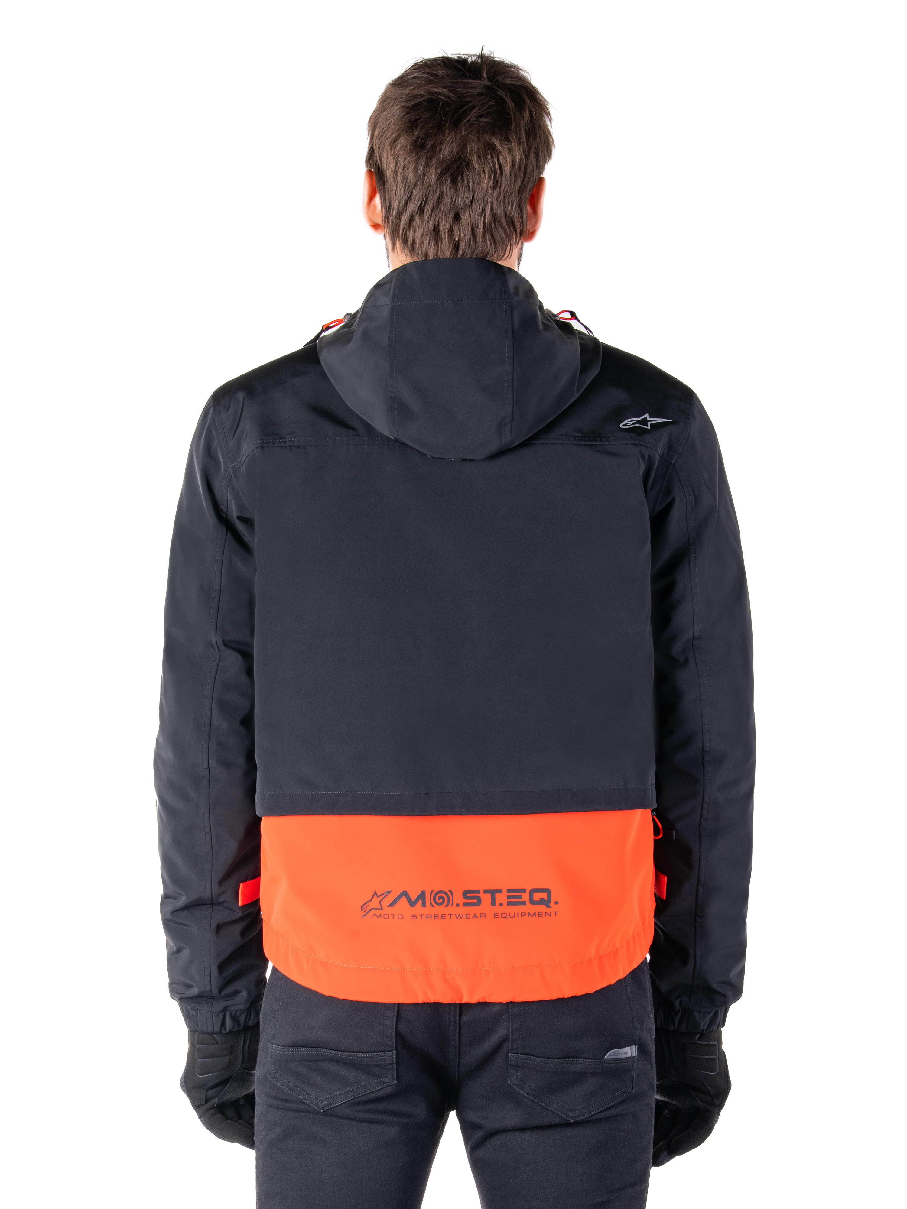 Alpinestars Mootant Waterproof Parka in Spicy Orange e nero, vista posteriore che mostra la parte superiore nera con cappuccio e il pannello inferiore arancione con il marchio MO.ST.EQ., streetwear funzionale da moto