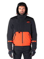 Alpinestars Mootant Waterproof Parka, giacca da moto, arancione e nero, design modulare per tutte le stagioni con cappuccio, tasche anteriori con zip e dettagli con cinturini arancioni sulle maniche, indossata da un modello con guanti e pantaloni neri