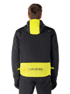 Alpinestars Mootant Waterproof Parka, giacca da moto, Lime Punch e nero, vista posteriore con design con cappuccio e marchio riflettente MO.ST.EQ. sulla parte inferiore della schiena, indossata con pantaloni da moto e guanti neri.