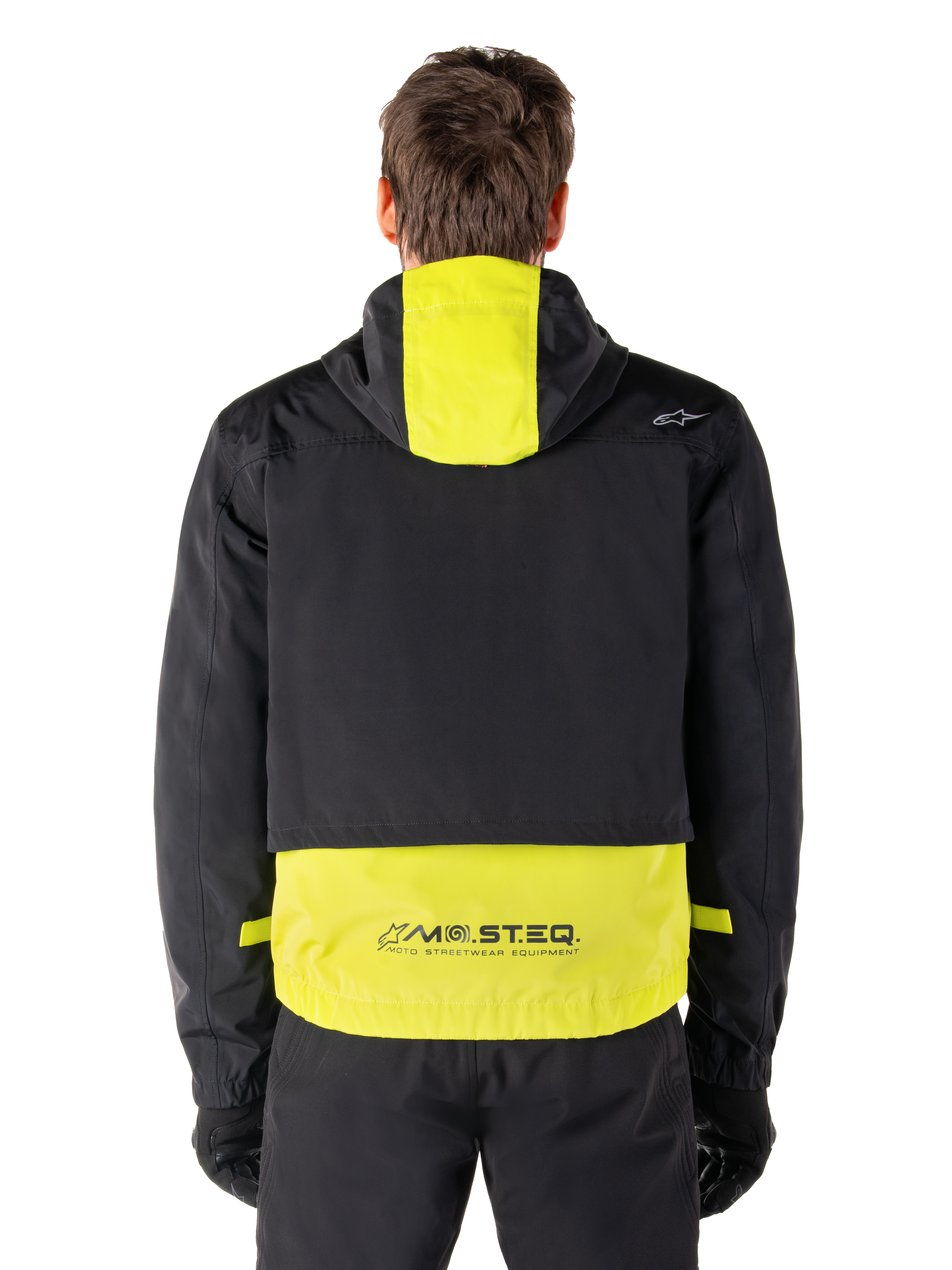 Alpinestars Mootant Waterproof Parka, giacca da moto, Lime Punch e nero, vista posteriore con design con cappuccio e marchio riflettente MO.ST.EQ. sulla parte inferiore della schiena, indossata con pantaloni da moto e guanti neri.
