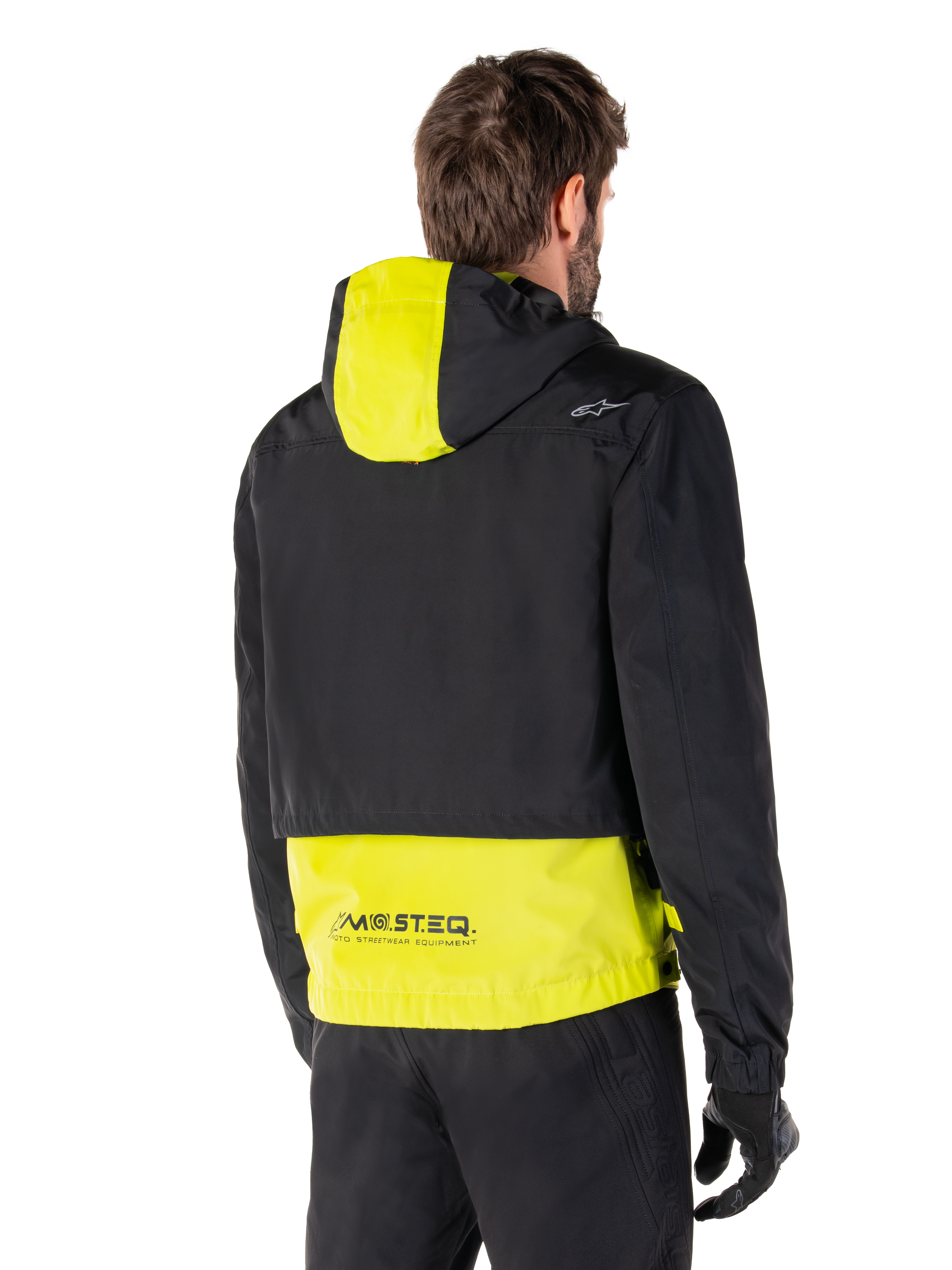 Alpinestars Mootant Waterproof Parka, vista posteriore, Lime Punch e nero, caratterizzato da una parte superiore nera con pannello del cappuccio e parte inferiore della schiena giallo lime, marchio MO.ST.EQ. sull'orlo, indossato con pantaloni da moto e guanti neri, giacca da moto urban contemporary