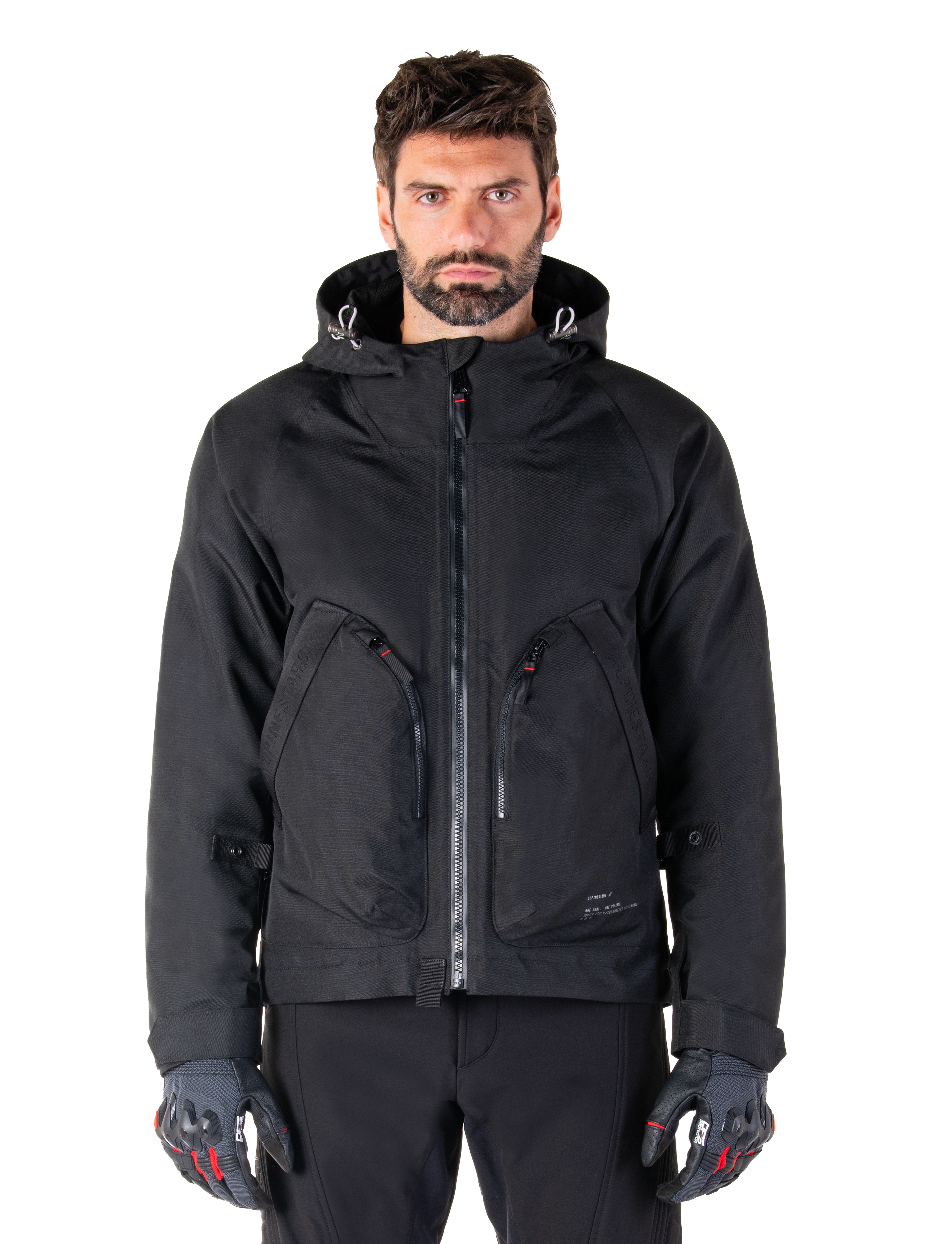 Alpinestars Morush Waterproof Parka, giacca da moto nera, design con cappuccio, zip frontale e due ampie tasche con cerniera, indossata con guanti neri e rossi, abbigliamento urban riding