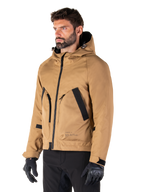 Alpinestars Morush Parka impermeabile, marrone (Utility Brown), modello maschile che indossa il parka con guanti da moto neri e pantaloni neri, design minimalista d'ispirazione streetwear con cappuccio a prova di maltempo e ampie tasche frontali, abbigliamento da moto impermeabile