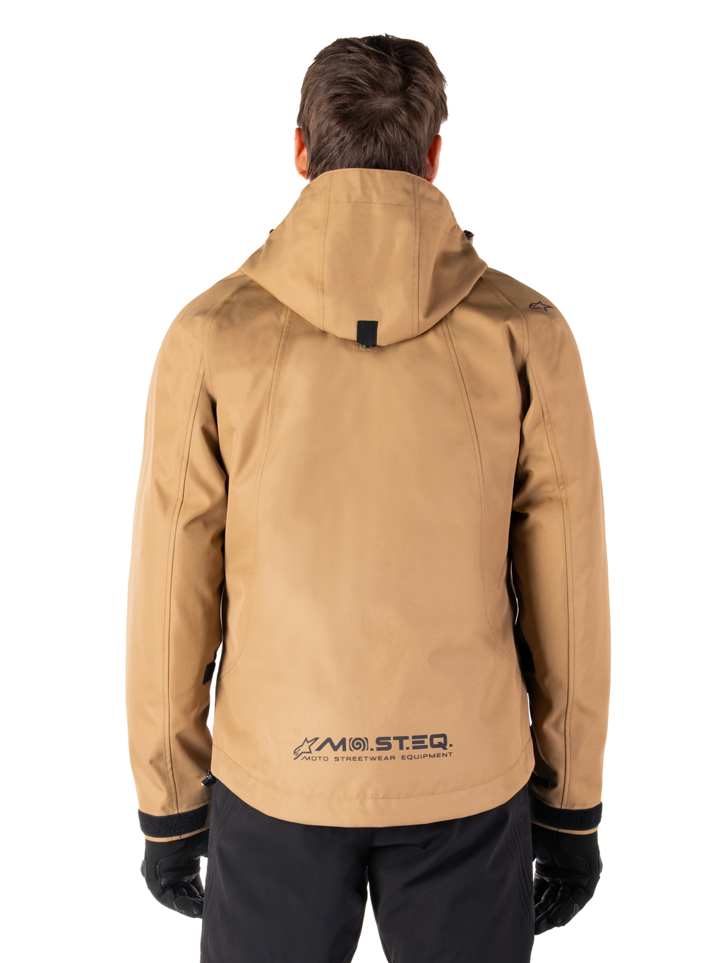 Parka impermeabile Alpinestars Morush, Utility Brown, vista posteriore, con cappuccio e marchio MO.ST.EQ. sulla parte inferiore della schiena, abbinato a pantaloni e guanti neri, abbigliamento da moto moderno ispirato allo streetwear