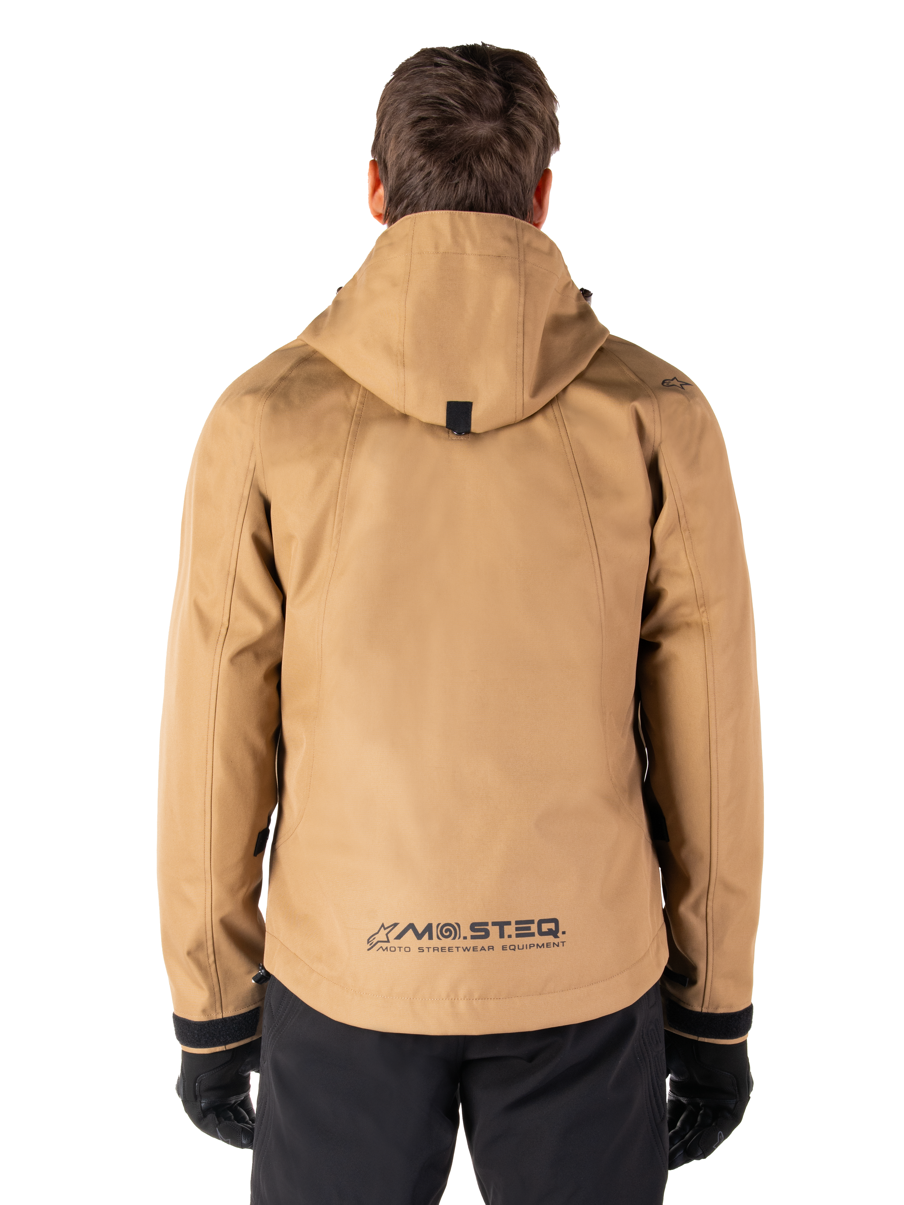 Parka impermeabile Alpinestars Morush, Utility Brown, vista posteriore, con cappuccio e marchio MO.ST.EQ. sulla parte inferiore della schiena, abbinato a pantaloni e guanti neri, abbigliamento da moto moderno ispirato allo streetwear