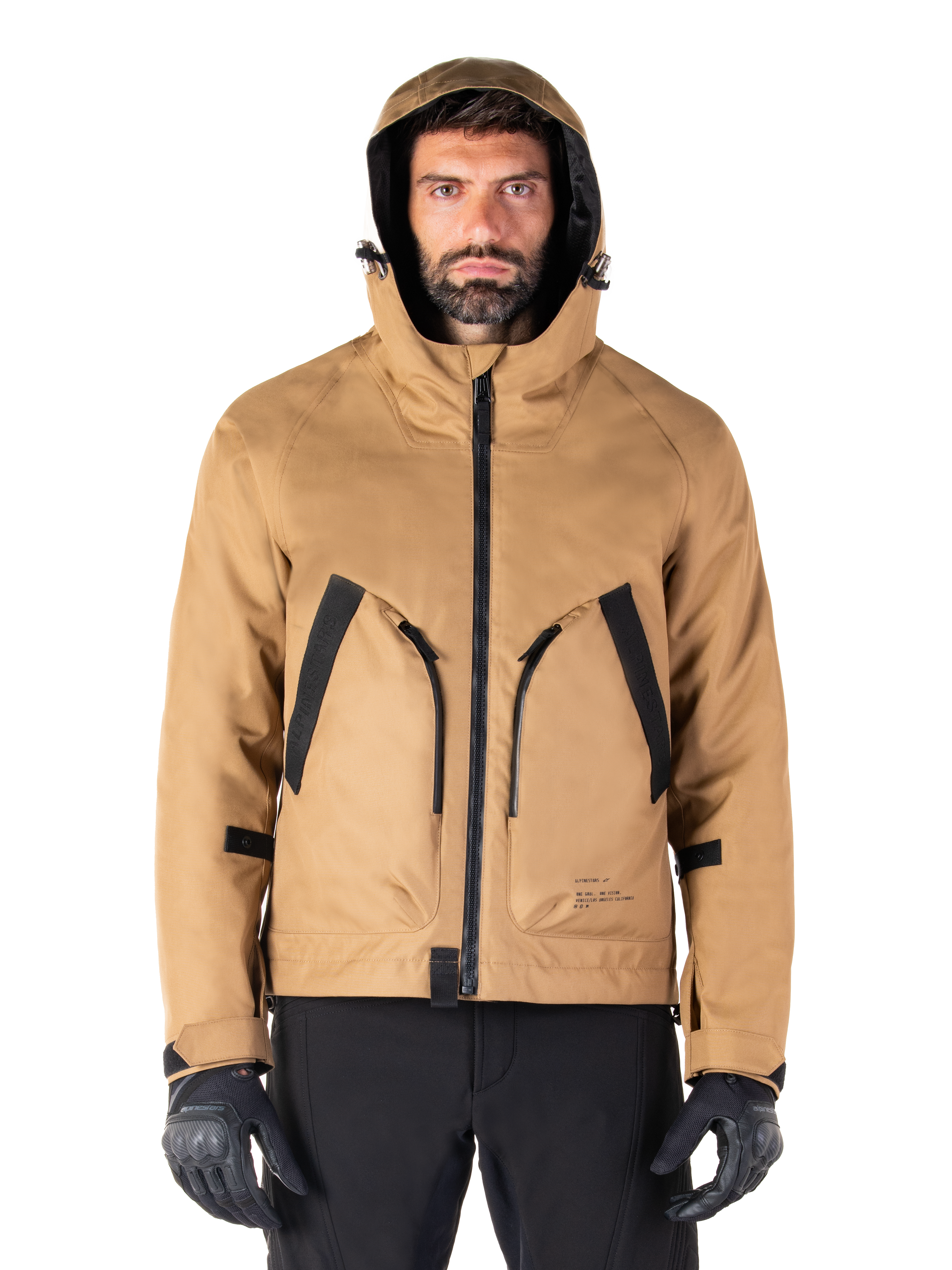 Alpinestars Morush Waterproof Parka, giacca da moto, marrone utility, design con cappuccio ispirato allo streetwear con ampie tasche anteriori con accenti neri, indossata con guanti da moto e pantaloni neri, abbigliamento moto urban contemporary