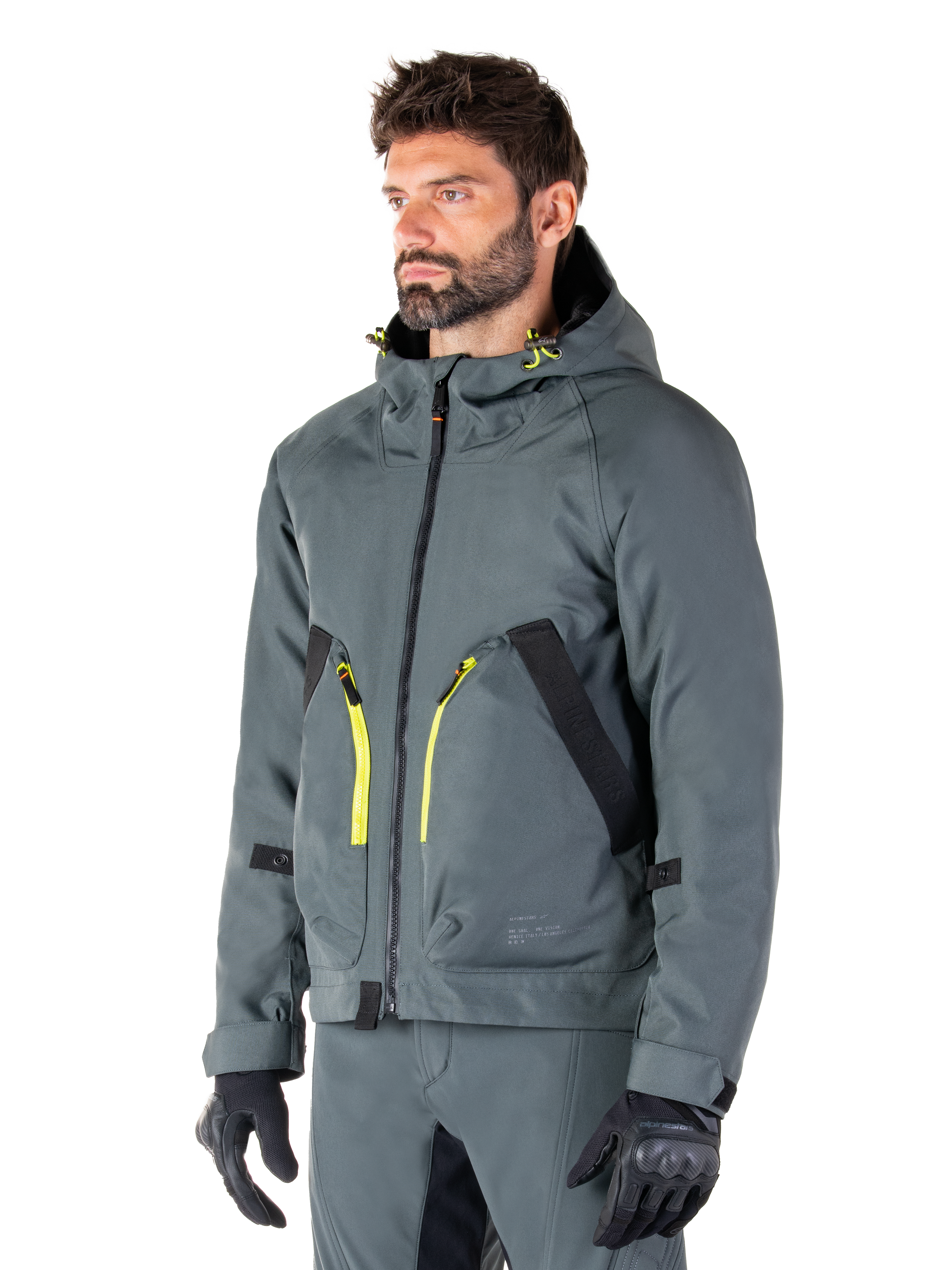 Alpinestars Morush Waterproof Parka, giacca da moto Urban Gray, design con cappuccio e dettagli delle zip in giallo acceso, rifiniture delle tasche nere, indossato con pantaloni da moto grigi coordinati e guanti neri, abbigliamento da moto contemporaneo ispirato allo streetwear.