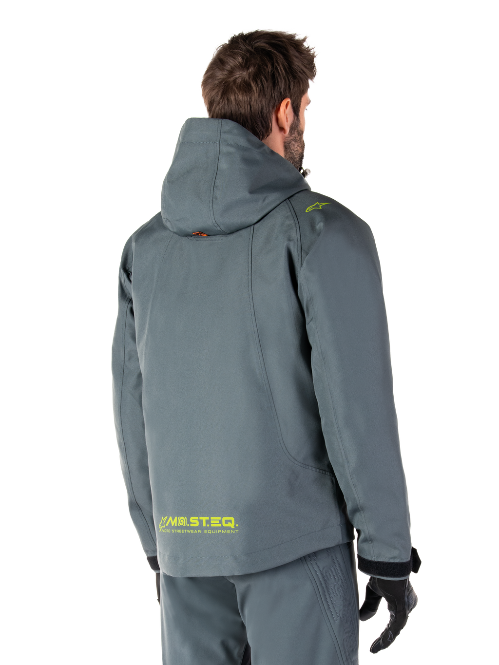 Alpinestars Morush Waterproof Parka in Urban Gray, vista posteriore, con marchio MO.ST.EQ. giallo sulla parte bassa della schiena e sulla spalla, design minimalista con cappuccio, indossato con pantaloni da moto grigi coordinati e guanti neri, abbigliamento urban streetwear da moto.