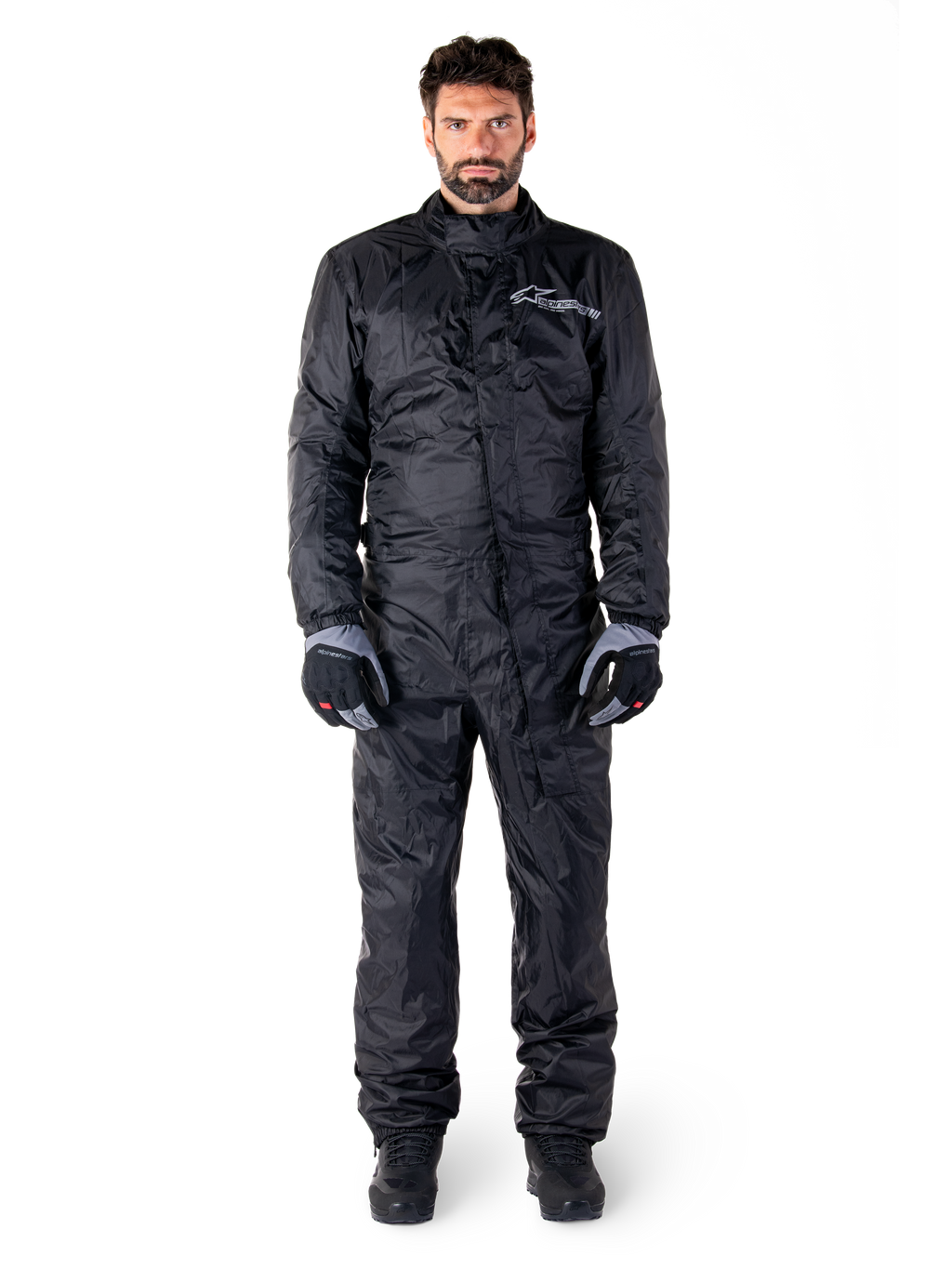Alpinestars Hurricane Rain V2 Suit, tuta antipioggia integrale da moto nera, abbigliamento protettivo impermeabile con collo alto e chiusura frontale antipioggia, con logo bianco sul petto, indossata con guanti e stivali neri e grigi