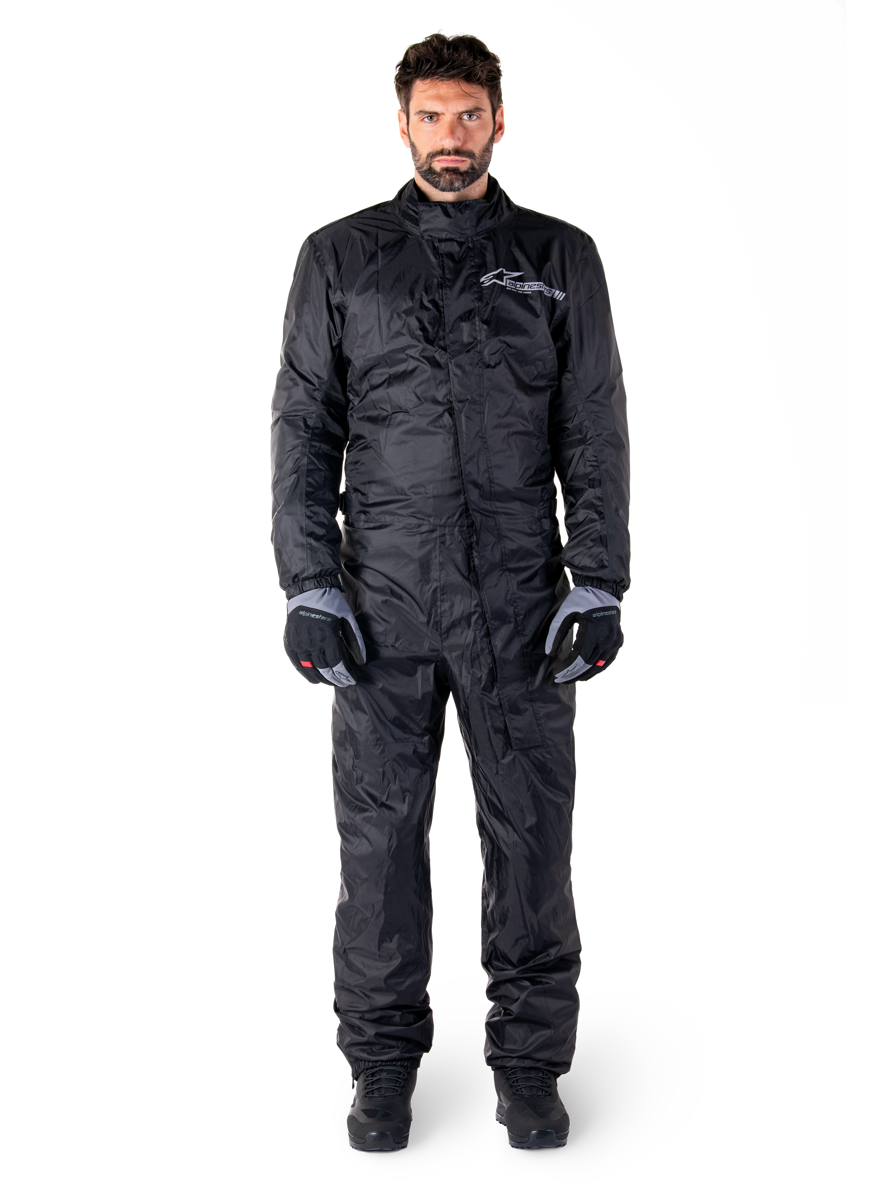 Alpinestars Hurricane Rain V2 Suit, tuta antipioggia integrale da moto nera, abbigliamento protettivo impermeabile con collo alto e chiusura frontale antipioggia, con logo bianco sul petto, indossata con guanti e stivali neri e grigi