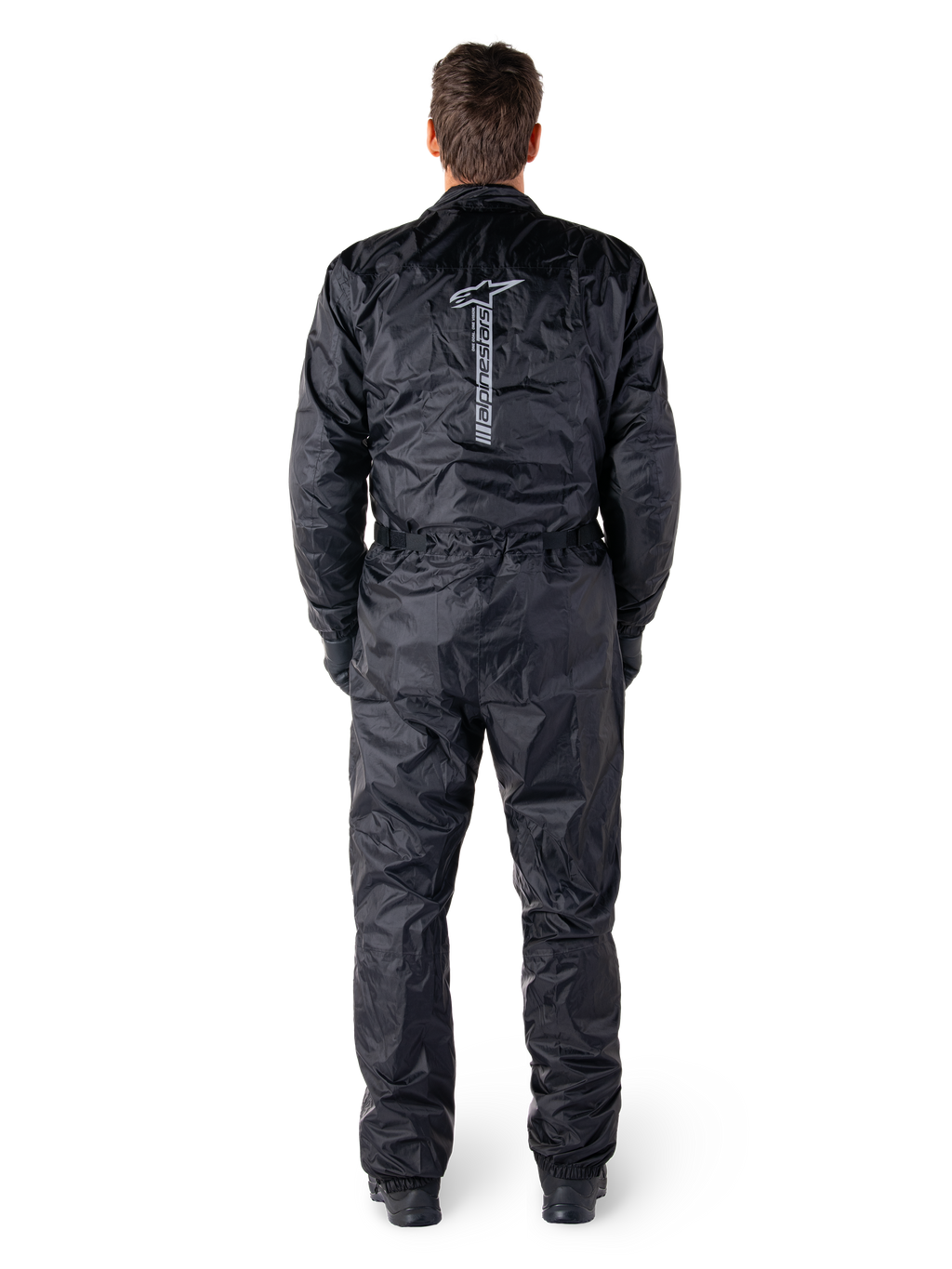 Tuta Alpinestars Hurricane Rain V2, tuta da moto intera impermeabile nera, vista posteriore che mostra il grande logo e la scritta Alpinestars in verticale, tessuto leggero stropicciato con vita e polsini elasticizzati, progettata per la protezione durante la guida in condizioni di bagnato.