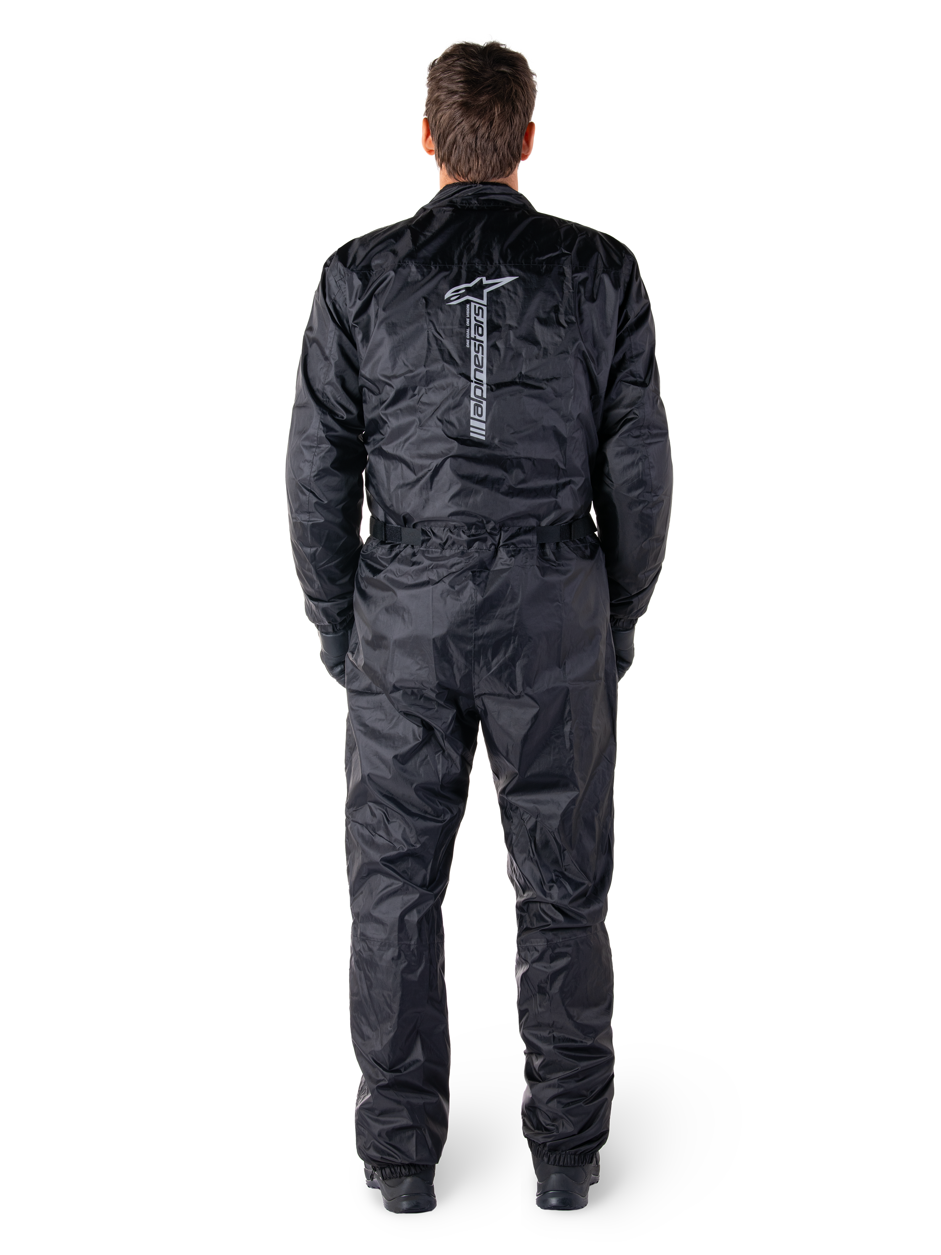 Tuta Alpinestars Hurricane Rain V2, tuta da moto intera impermeabile nera, vista posteriore che mostra il grande logo e la scritta Alpinestars in verticale, tessuto leggero stropicciato con vita e polsini elasticizzati, progettata per la protezione durante la guida in condizioni di bagnato.