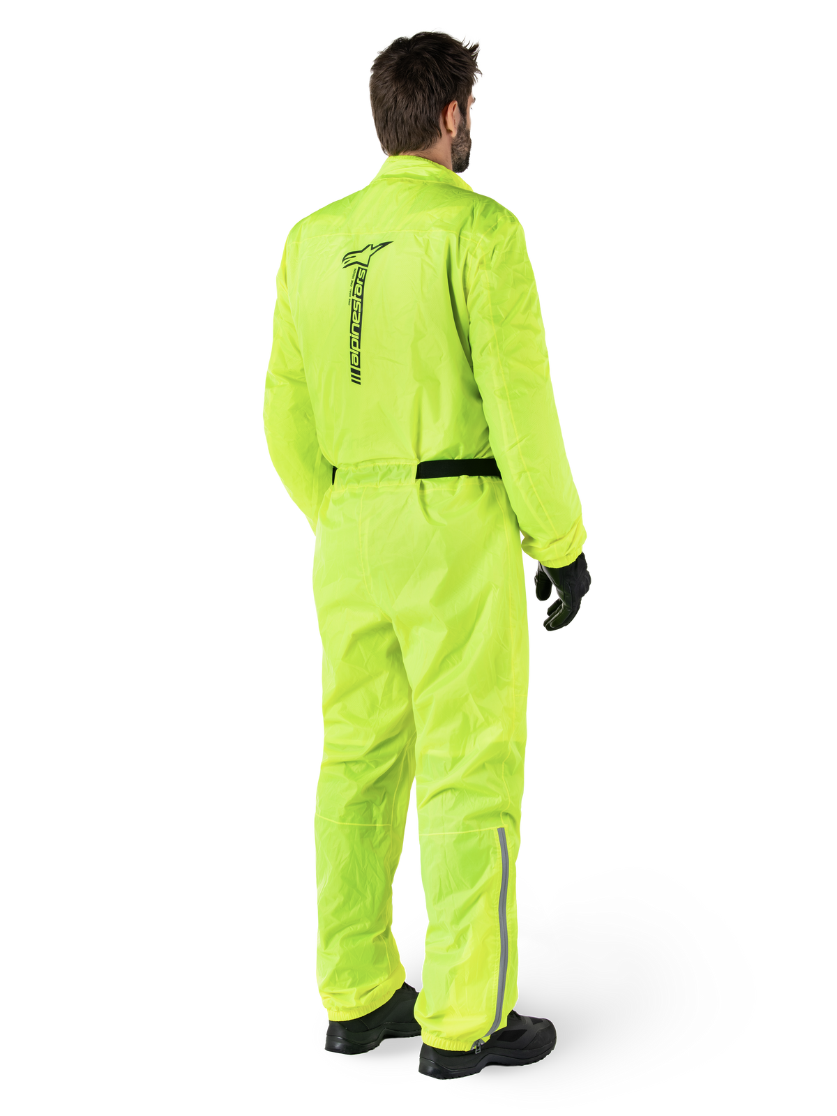 Alpinestars Hurricane Rain V2 Suit, Giallo Fluo, vista posteriore di un pilota che indossa una tuta antipioggia da moto intera, con logo Alpinestars nero sulla schiena, cintura nera in vita e strisce riflettenti sulla parte inferiore delle gambe, indossata con guanti e stivali neri