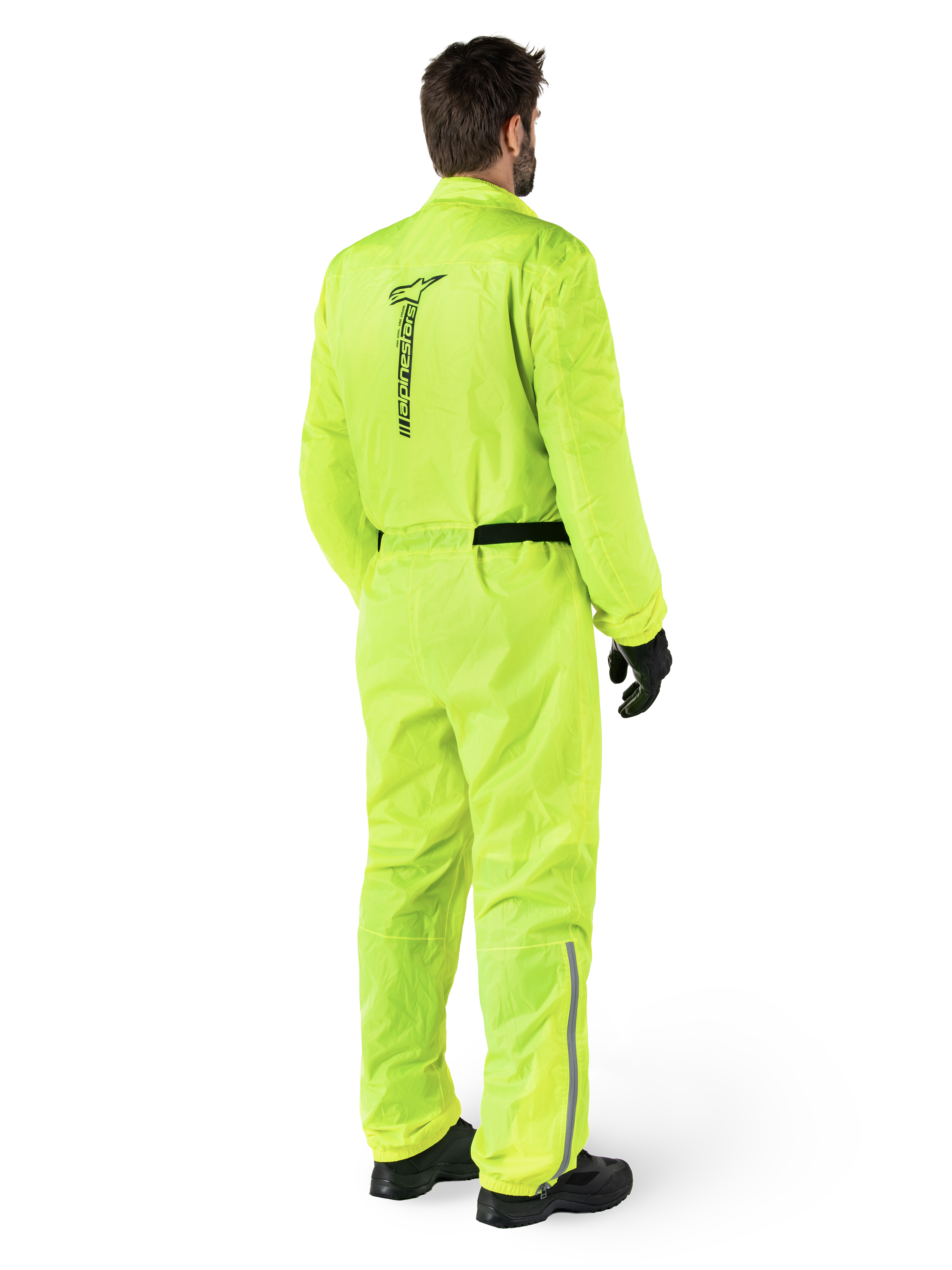 Alpinestars Hurricane Rain V2 Suit, Giallo Fluo, vista posteriore di un pilota che indossa una tuta antipioggia da moto intera, con logo Alpinestars nero sulla schiena, cintura nera in vita e strisce riflettenti sulla parte inferiore delle gambe, indossata con guanti e stivali neri