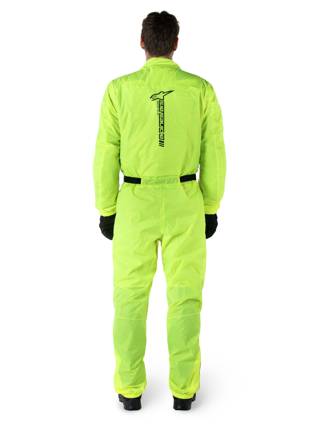 Tuta Alpinestars Hurricane Rain V2, tuta antipioggia da moto intera, giallo fluo, vista posteriore con marchio Alpinestars nero verticale, vita e polsini elasticizzati, indossata con guanti e stivali neri, abbigliamento tecnico impermeabile e antivento