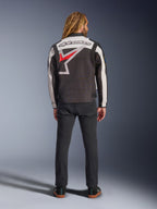 Giacca Alpinestars Axton, giacca da moto, nero, bianco sporco e rosso brillante, vista posteriore su un modello, con un grande logo a stella Alpinestars sul retro, pannelli delle maniche bianco sporco, indossata con pantaloni neri, design ispirato all'abbigliamento racing vintage