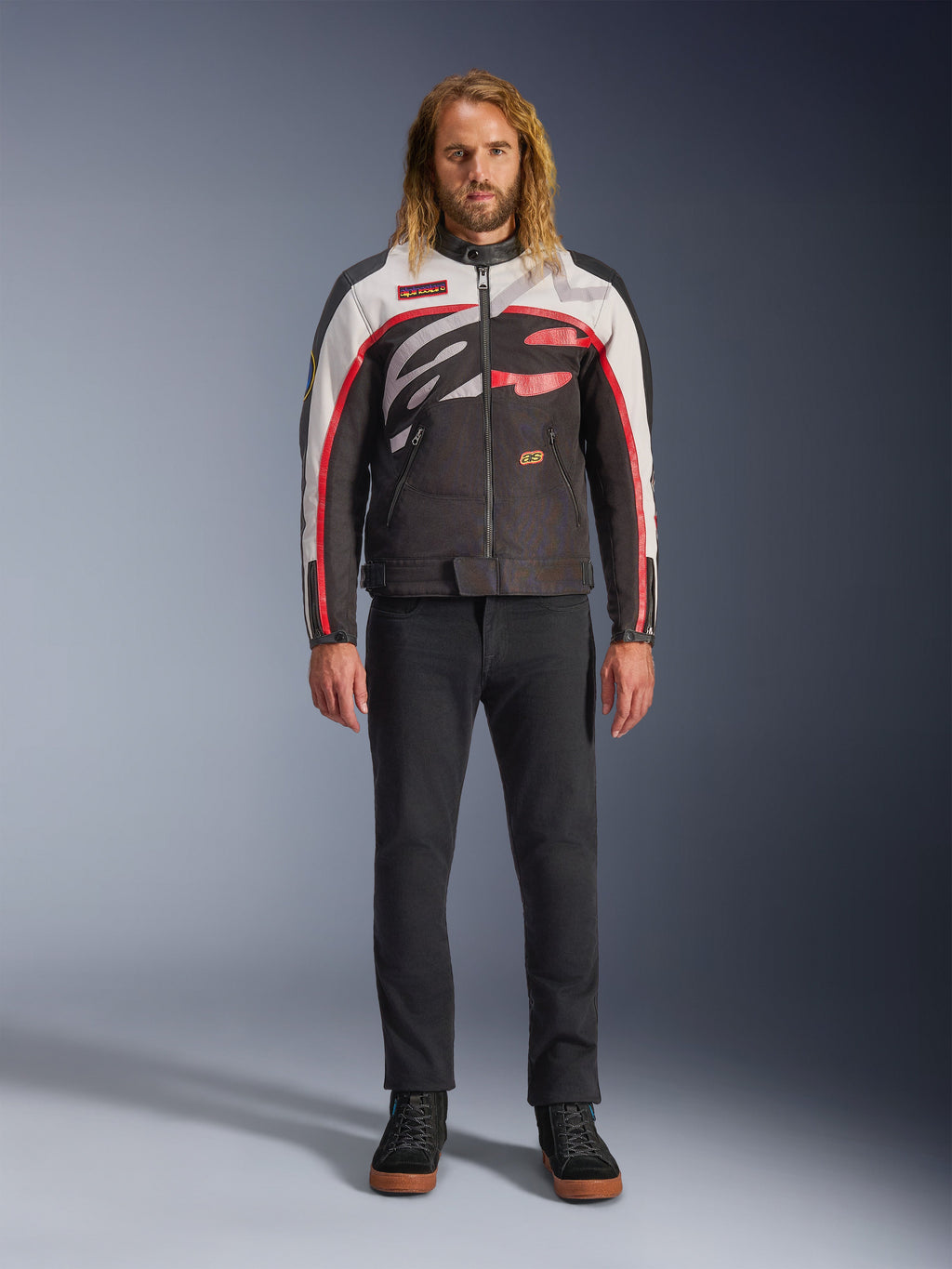 Giacca Alpinestars Axton, giacca da moto, nero, bianco sporco e rosso acceso, indossata da un modello con pantaloni neri e sneakers, con un audace logo avvolgente e un design d'ispirazione racing vintage