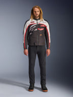 Giacca Alpinestars Axton, giacca da moto, nero, bianco sporco e rosso acceso, indossata da un modello con pantaloni neri e sneakers, con un audace logo avvolgente e un design d'ispirazione racing vintage