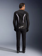 Giacca Alpinestars AST V3 Air, vista posteriore, nero e grigio scuro con accenti bianchi, con grande logo Astar bianco sulla parte inferiore, strisce riflettenti sul retro e costruzione in tessuto mesh, indossata con pantaloni e stivali neri per un look sportivo
