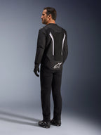 Alpinestars AST V3 Air Jacket, giacca da moto nera e bianca, vista posteriore su modello, con inserti in mesh per il flusso d'aria e logo bianco sulla parte inferiore della schiena, indossata con abbigliamento tecnico da guida nero