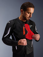 Giacca Alpinestars AST V3 Air in nero, uomo che mostra un inserto protettivo per il torace rosso acceso con motivo a nido d'ape, evidenziando la compatibilità Tech-Air Ready e la protezione interna integrata per la sicurezza motociclistica.