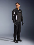 Alpinestars AST V3 Air Jacket, nera con accenti e logo bianchi, giacca da moto leggera con ventilazione in mesh, indossata da un uomo con pantaloni da guida, guanti e scarpe neri, abbigliamento tecnico estivo per guida sportiva e urbana.