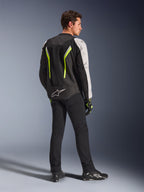 Giacca Alpinestars AST V3 Air in Nero Argento Giallo Fluo, giacca da moto in tessuto indossata da un pilota uomo vista da dietro, con ampi pannelli in mesh e accenti giallo fluorescente, abbinata a pantaloni da moto neri, guanti neri e scarpe Alpinestars nere, equipaggiamento tecnico per la guida sportiva.