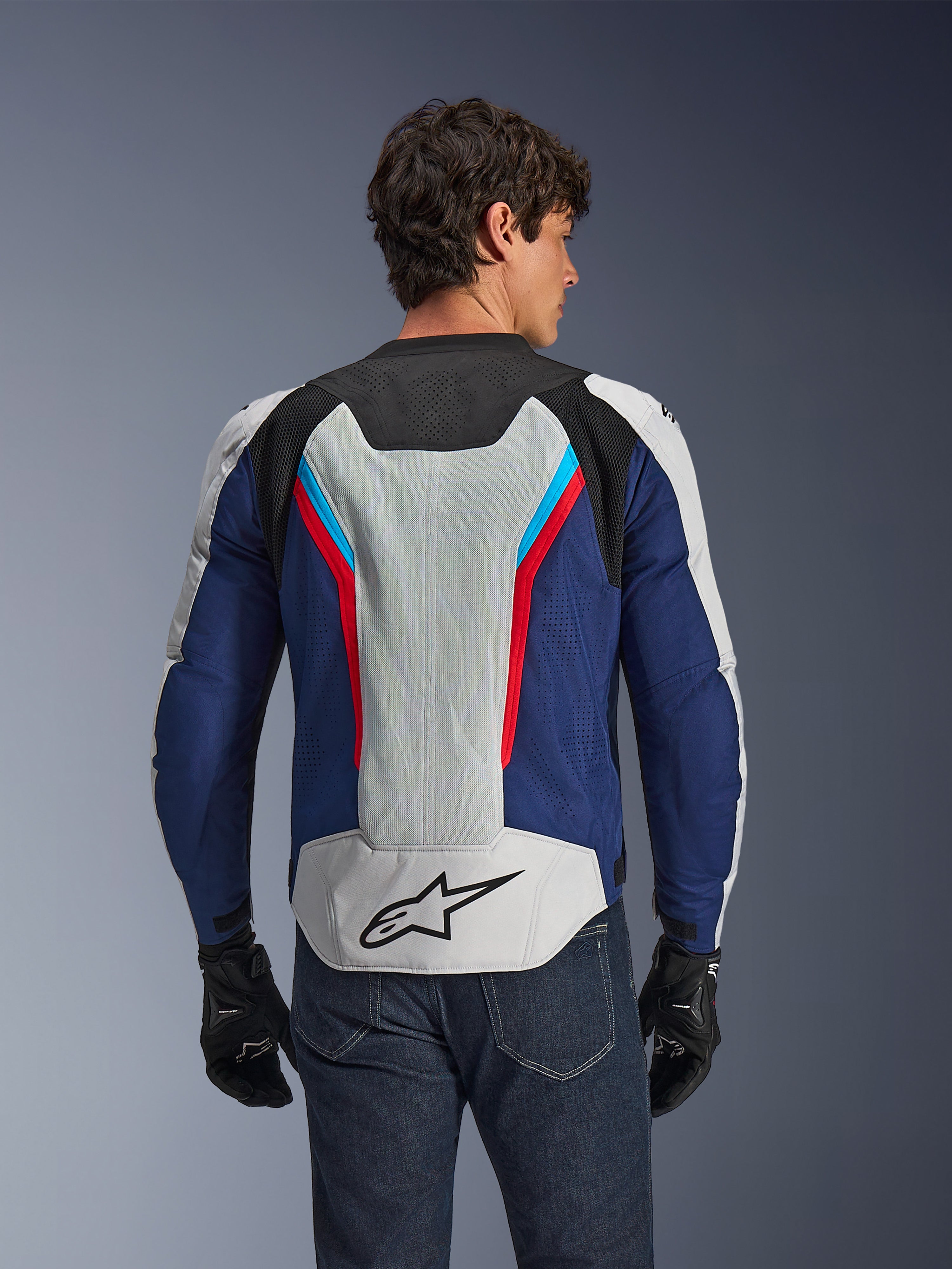 Giacca Alpinestars AST V3 Air, giacca da moto, colore Silver Deep Blue Bright Red, vista posteriore indossata da un pilota, con pannelli in rete tecnica e perforazioni laser per la ventilazione, logo a stella nero sulla parte bassa della schiena, design sportivo per climi caldi