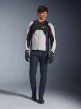 Modello uomo con giacca Alpinestars AST V3 Air in Silver Deep Blue Bright Red, caratterizzata da ventilazione in rete e pannelli traforati, abbinata a jeans da moto in denim scuro e guanti neri, equipaggiamento sportivo da moto per il clima caldo.