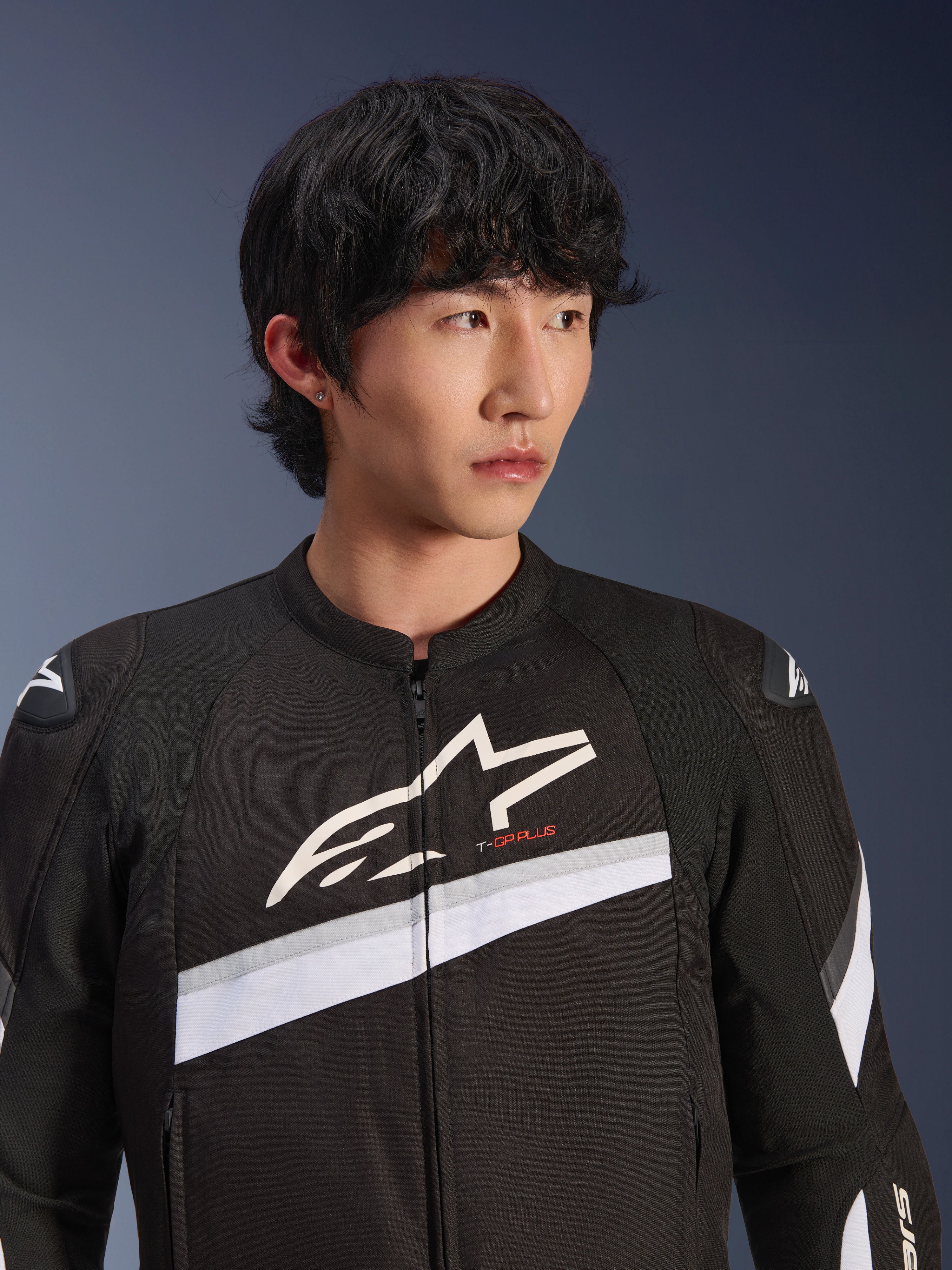 Giacca Alpinestars T-GP Plus R V4, nero e bianco, giacca da moto in tessuto indossata da un modello, con un grande logo a stella bianco sul petto, strisce diagonali bianche e protezioni per le spalle DFS Lite, abbigliamento da strada d'ispirazione sportiva