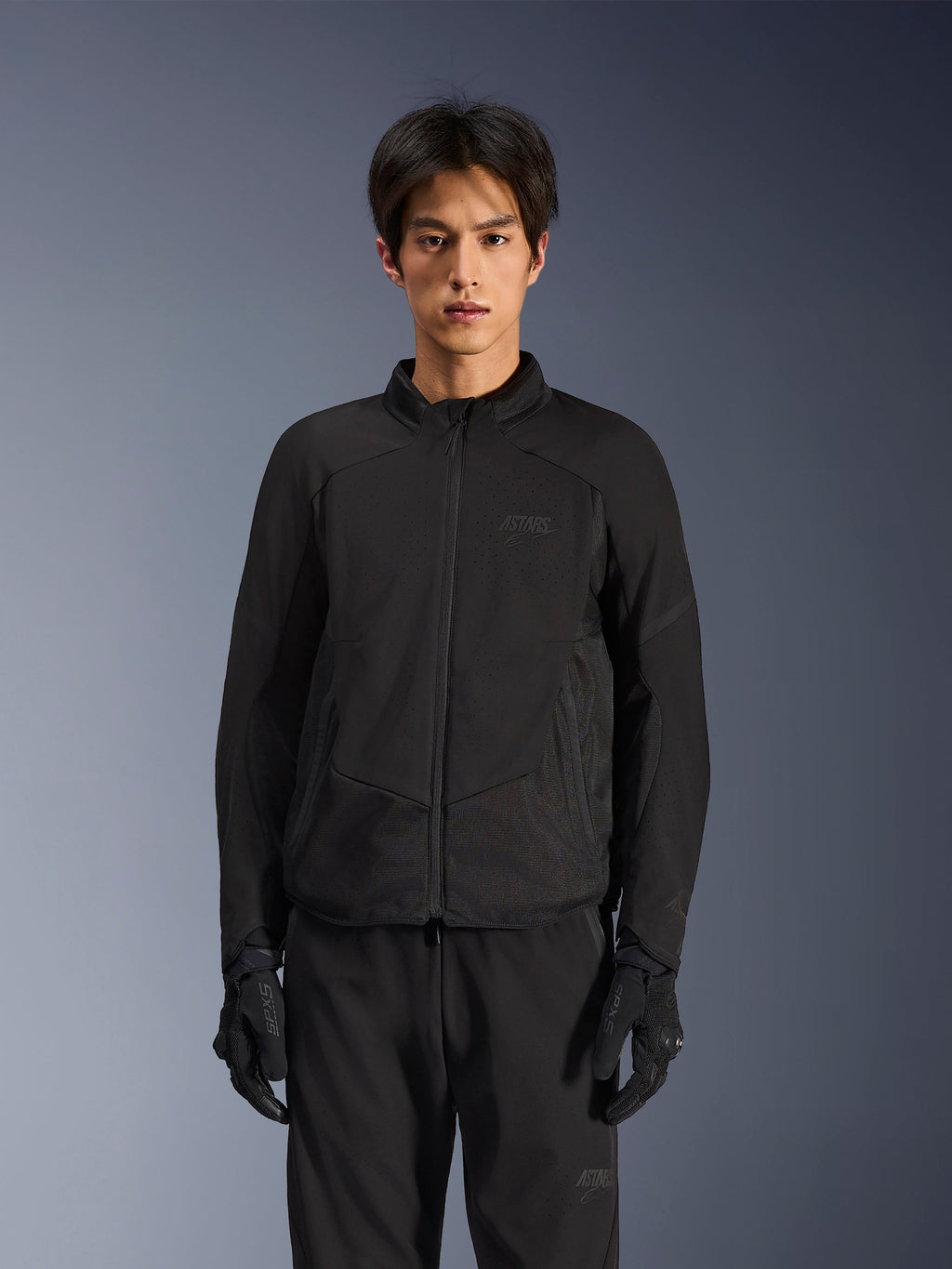 Giacca Alpinestars Aeroshell Airflow in Nero Antracite, giacca da moto leggera con ventilazione traforata al laser su petto e maniche, pannelli in rete traspirante e un elegante design dal taglio sportivo, indossata da un modello con guanti da moto neri.