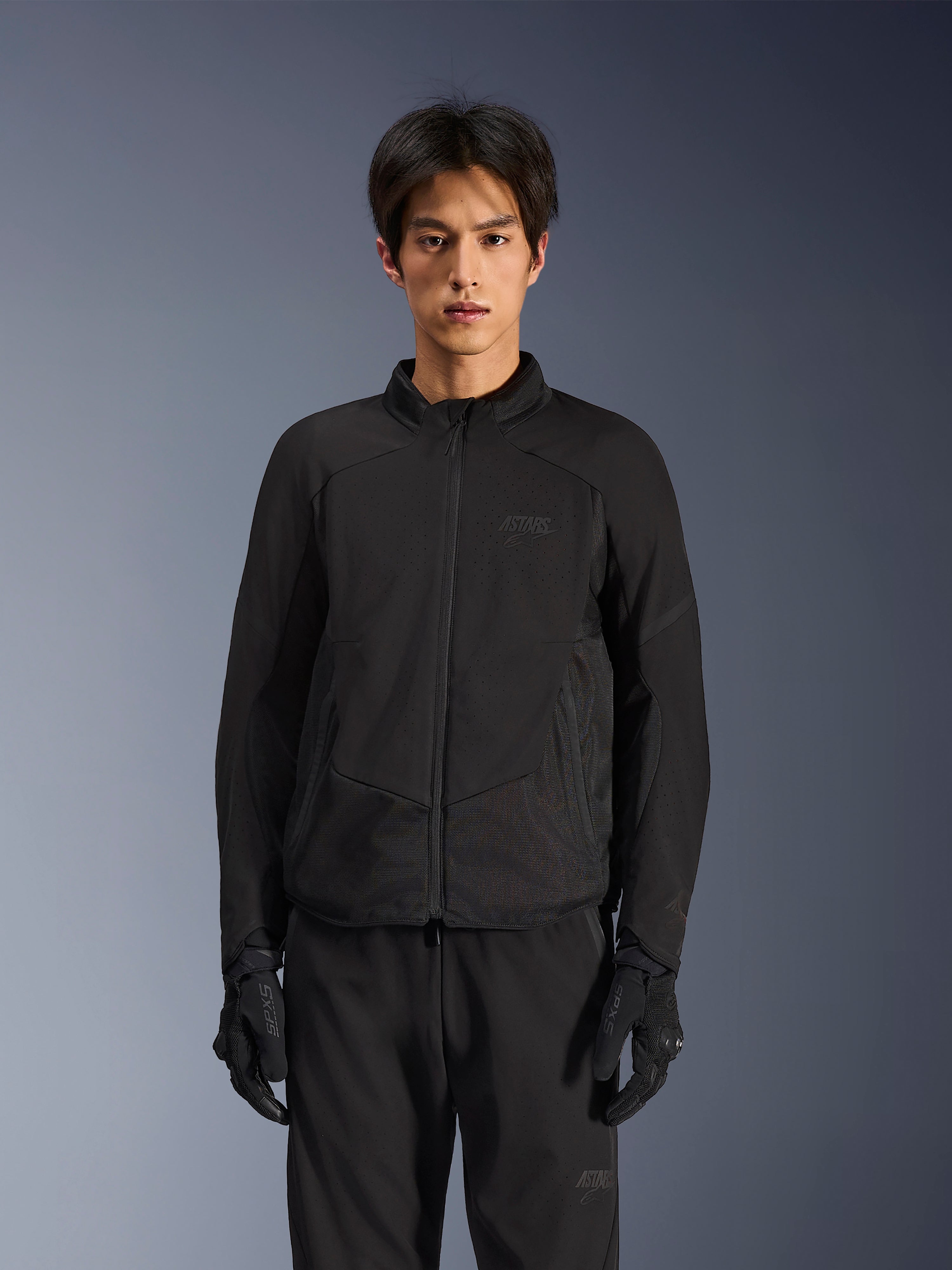 Giacca Alpinestars Aeroshell Airflow in Nero Antracite, giacca da moto leggera con ventilazione traforata al laser su petto e maniche, pannelli in rete traspirante e un elegante design dal taglio sportivo, indossata da un modello con guanti da moto neri.