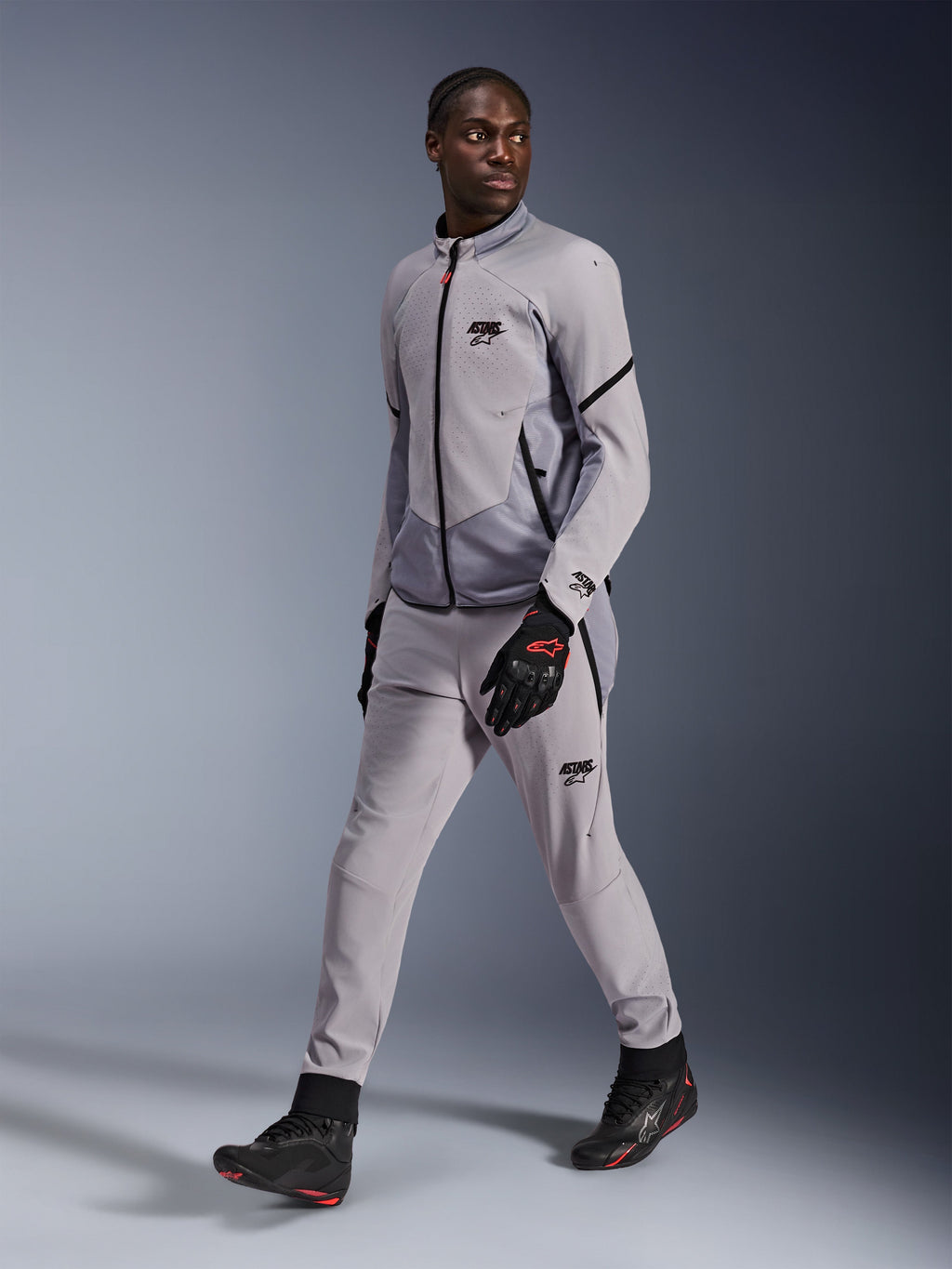 Giacca Alpinestars Aeroshell Airflow in Mid Gray Anthracite, indossata da un modello con pantaloni da moto grigi coordinati e guanti neri, caratterizzata da ventilazione sul petto perforata al laser e design dal taglio sportivo.