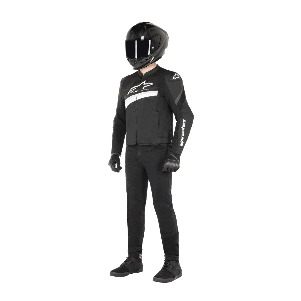 Motociclista con indosso la giacca Alpinestars T-GP Plus R V4 Airflow in nero e bianco, giacca da moto in tessuto con pannelli in rete e logo Alpinestars bianco, abbinata a un casco nero, guanti da moto neri, pantaloni neri e scarpe nere