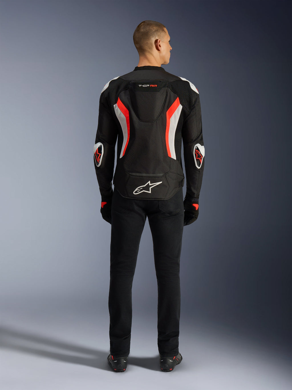 Giacca Alpinestars T-GP Air, giacca da moto, Nero Rosso Fluo, vista posteriore su un modello, dotata di gobba aerodinamica, accenti bianchi e rosso fluorescente, logo Alpinestars sulla parte inferiore della schiena, design dal taglio sportivo per guida su strada.