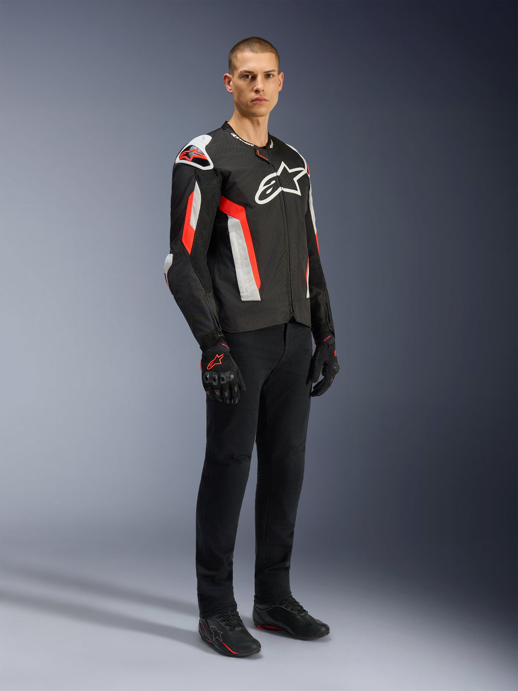 Giacca Alpinestars T-GP Air, Nero Rosso Fluo, indossata da un modello con pantaloni da moto e guanti neri, caratterizzata da pannelli in tessuto perforato al laser, logo Alpinestars bianco e accenti rossi, giacca da moto sportiva per la guida su strada in climi caldi