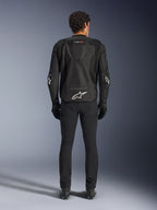 Alpinestars T-GP Air Jacket, giacca da moto in tessuto, nera, vista posteriore di un uomo con pannelli di ventilazione in rete, una gobba aerodinamica e loghi Alpinestars bianchi sulla parte inferiore della schiena e sui gomiti, indossata con pantaloni da guida e guanti neri