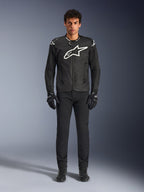 Alpinestars T-GP Air Jacket, giacca da moto in tessuto nero con un grande logo Astars bianco sul petto, indossata da un modello con pantaloni da guida e guanti neri, con pannelli traforati e ventilazione in rete per la guida sportiva