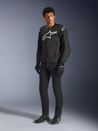Alpinestars T-GP Air Jacket, giacca da moto in tessuto nero, indossata da un modello con pantaloni e guanti neri coordinati, con un evidente logo Alpinestars bianco sul petto e sulle spalle, pannelli in mesh ventilati e una vestibilità sportiva di derivazione racing