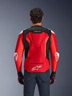 Giacca Alpinestars T-GP Air, giacca da moto in tessuto, rosso acceso e nero con accenti bianchi, vista posteriore che mostra la gobba aerodinamica e i pannelli di ventilazione in mesh, con logo Alpinestars e branding T-GP Air, indossata con jeans scuri e guanti da corsa