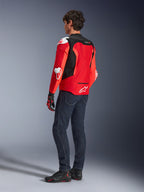 Giacca Alpinestars T-GP Air, vista posteriore di un uomo che indossa una giacca in tessuto rosso brillante e rosso fluo con pannelli in mesh nero e slider bianchi, abbinata a jeans blu scuro e scarpe da moto nere, abbigliamento tecnico da moto sportiva.