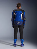 Giacca Alpinestars T-GP Air, Bright Blue Navy White, vista posteriore con gobba aerodinamica e pannelli di ventilazione in mesh, logo Alpinestars bianco sulla parte inferiore della schiena, indossata con pantaloni neri e stivali racing blu