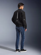 Modello che indossa la giacca Alpinestars Flight Air nera, vista dal retro, abbinata a jeans da moto blu e sneakers nere, con logo Alpinestars bianco verticale e pannelli di ventilazione in mesh 3D.