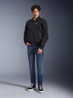 Modello che indossa la giacca Alpinestars Flight Air in nero, una giacca da moto urbana in stile bomber con pannelli in mesh 3D e cerniera frontale, abbinata a jeans blu e sneakers nere, abbigliamento da guida contemporaneo d'ispirazione street.